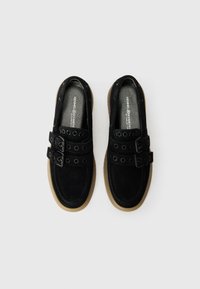 Chaussures en suede noir avec des accents de double boucle, dotées de découpes circulaires et d'une semelle en caoutchouc. Texture lisse et design en pointe arrondie.