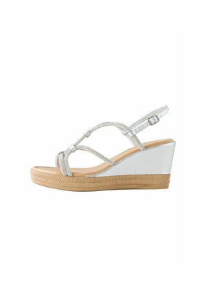 Valge kiilkontsaga sandaal beežapruuni tallaga, metallik-hõbedaste rihmade ja reguleeritava pahkluu pandlaga, külgvaates valgel taustal.