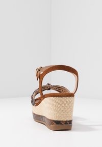 Sandalia de cuña de ante marrón con plataforma de yute trenzado, tira en el tobillo y detalles decorativos trenzados. Presenta un diseño texturizado multicolor.