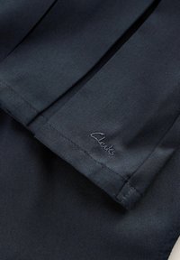 Jūras zilas krāsas audums, kurā ir pleitu dizains ar teksturētu apdari. Tajā ir maigs izšūts "Clarks" logo malā.