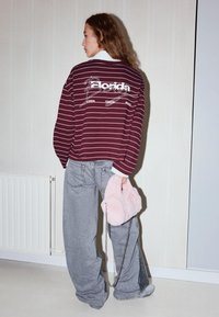 Bordó és fehér csíkos, túlméretezett pulóver "Florida" felirattal, világosszürke farmerrel és egy puha rózsaszín műszőrme borítójú táskával párosítva.