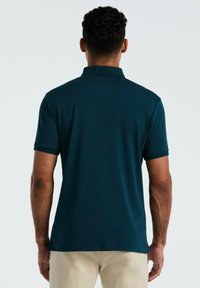 Polo shirt bleu marine avec des manches courtes et un col remonté, présentant une texture lisse et des détails de couture subtils le long de l'ourlet.