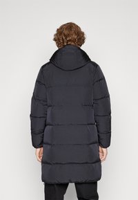 Zwarte pufferjas met capuchon, voorzien van een geborduurd ontwerp, lange mouwen en een knielange snit. Soepele textuur en minimalistische stijl.