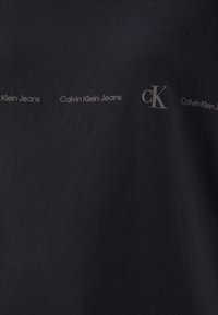 Camiseta de algodón azul marino con una textura suave. Presenta un logotipo repetido en gris claro: "Calvin Klein Jeans" y "CK" en varias ubicaciones.