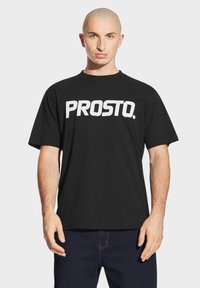 Czarny bawełniany t-shirt z wyrazistym białym napisem "PROSTO." na przodzie. Krótkie rękawy i luźny krój. Minimalistyczny design.