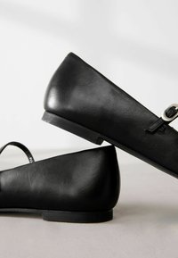 Bailarinas de cuero negro con textura suave, punta redondeada y un pequeño acento de hebilla en una tira. Diseño simple, sin patrones, forma minimalista.