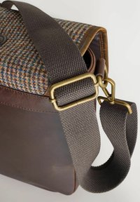 Brown leather bag with a tweed flap. Features a textured, dark fabric strap and brass hardware. Compact shape, functional design.