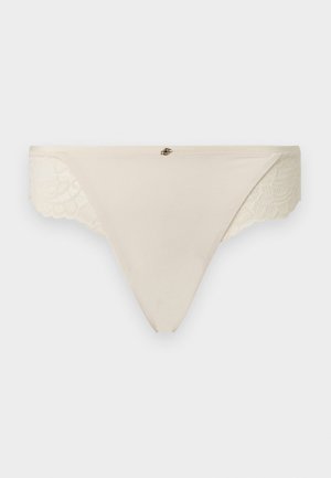 Beige women's thong underwear with lace side panels and a small decorative metal accent at the center waistband.