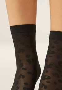Černé průsvitné kotníkové ponožky s jemným leopardím potiskem a pevnou černou elastickou manžetou nahoře pro jisté uchycení.