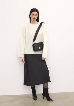 Maglione crema accogliente, gonna midi in satin nera, stivali alla caviglia neri con punte lucide e una borsa a tracolla nera strutturata con una tracolla decorativa.
