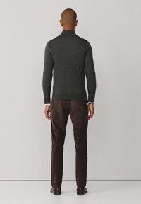 Dunkelgrüner Pullover mit langen Ärmeln, taillierter Passform und Stehkragen, kombiniert mit dunkelbraunen Slim-Fit-Hosen und schwarzen Schuhen.
