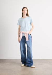 Svetlomodré bavlnené tričko s okrúhlym výstrihom, skombinované so širokými denimsovými džínsami a ružovým pleteným sveterom, ktorý má previazaný okolo pásu.