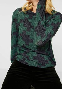 Långärmad topp med ett texturerat tyg i ett geometriskt mönster i grönt och mörkblått. Passformen är ledig med en rund halsringning.