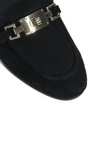 Zwarte suede loafers met een metallic gespaccent. Het ontwerp is gestroomlijnd met een ronde neus en gestikte details langs de rand.