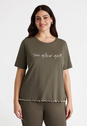 T-shirt verde oliva a maniche corte con la scritta "You glow girl" in strass e orlo con perle. Tessuto morbido con scollatura tonda.