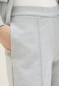 Lichtgrijze tapered broek van een zachte, textuurachtige stof. Beschikt over een zijzak en nette stiksels langs de naden, wat zorgt voor een verzorgde uitstraling.