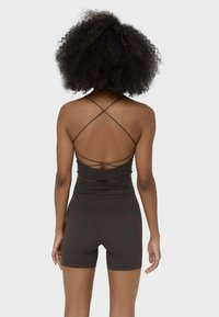 Set di abbigliamento sportivo marrone scuro composto da un top aderente con spalline incrociate e pantaloni corti a vita alta, realizzato in materiale liscio ed elastico.