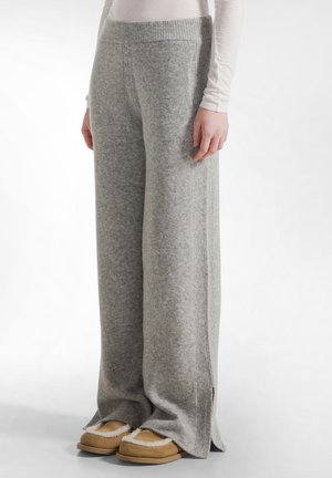 Grijze wollen wide-leg broek met geribde tailleband en zijsplitten, gecombineerd met tan slippers. Zachte textuur en losse pasvorm.