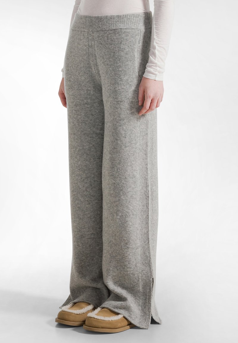 Grijze wollen wide-leg broek met geribde tailleband en zijsplitten, gecombineerd met tan slippers. Zachte textuur en losse pasvorm.