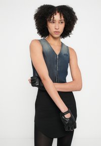 Farmer anyagtól készült ujjatlan felső V-nyakkivágással és cipzáros záródással, kék logóval ellátott folttal, fekete testhez simuló szoknyával és ujjatlan fekete kesztyűkkel párosítva.