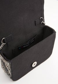 Clutch bag in tessuto nero con superficie texturizzata, tracolla in catena argentata e chiusura a scatto. L'interno presenta un'etichetta del marchio e una tasca interna.