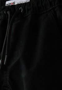Un short en tissu noir avec une taille élastique, des cordons de serrage réglables et des embouts métalliques, présentant une surface lisse et texturée.