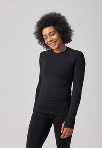Zwarte lange mouwen top van rekbaar materiaal, met een ronde hals, aansluitend design en schone naden. Het model draagt een bijpassende zwarte legging.