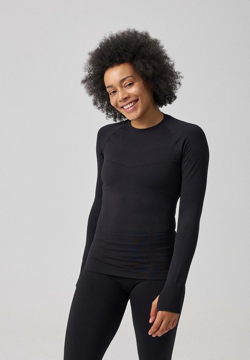 Zwarte lange mouwen top van rekbaar materiaal, met een ronde hals, aansluitend design en schone naden. Het model draagt een bijpassende zwarte legging.