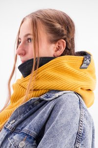Yellow knitted scarf with a textured pattern, layered over a black top, worn with a blue denim jacket, featuring a brand tag on the scarf.