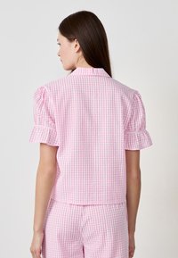 Pink gingham short-sleeve blouse with puffed sleeves. Made of lightweight fabric, featuring a collar and cropped design.
