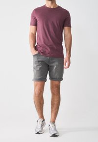 T-shirt bordeaux à manches courtes associé à un short en denim gris avec des revers. Les chaussures présentent un design blanc et noir avec des accents jaunes.