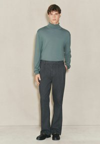 Green long-sleeve turtleneck sweater paired with dark gray tailored pants, featuring a smooth texture and a classic fit. Black shoes complete the look.