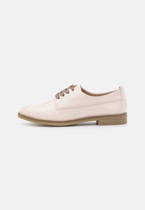 Skinnende lys beige snørestøvle i oxford-stil med brun sål og lav stablet hæl, vist fra siden på en ensfarvet hvid baggrund.