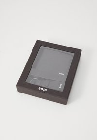 Black gift box with transparent front displays a wallet and keychain. The logo "BOSS" is printed in white on the packaging.