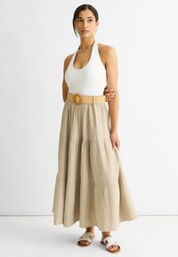 Top halter crema abbinato a una gonna a strati beige in tessuto texturizzato. La gonna presenta una cintura larga color tan con una fibbia circolare.