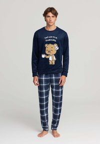 Il set di pigiama in felpa blu navy presenta una grafica di un orso, la scritta "Non svegliarmi" e pantaloni a scacchi nei colori blu, bianco e navy. Texture morbida.