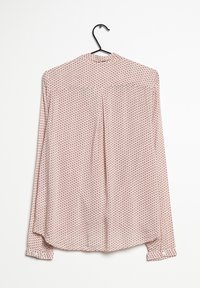 Blusa a maniche lunghe appesa a un gancio, realizzata in un tessuto rosa chiaro con un motivo a piccole pois ripetute in rosa scuro, e un orlo arrotondato.