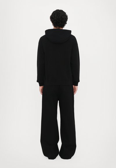 Felpa nera con cappuccio, vestibilità comoda e polsini a coste, abbinata a pantaloni neri a gamba larga con tasche posteriori. Design minimalista.
