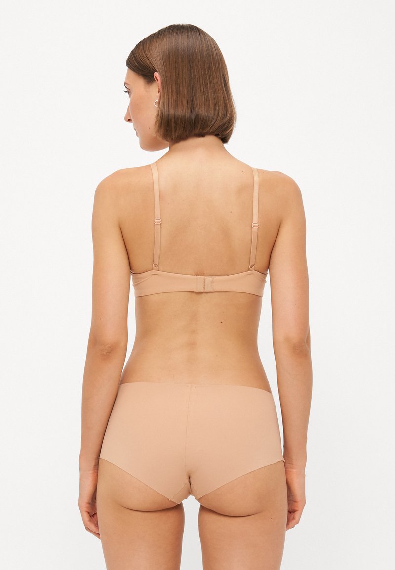 Beżowy biustonosz i dopasowany zestaw bielizny. Gładki materiał, regulowane ramiączka i bezszwowy design z pojedynczym zapięciem na plecach.