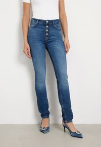 Kõrge vöökohaga sinised denim teksad, millel on kulunud viimistlus, viie esipaknaga ja kitsas sobivus. Kombineeritud terava ninaga kontsadega.