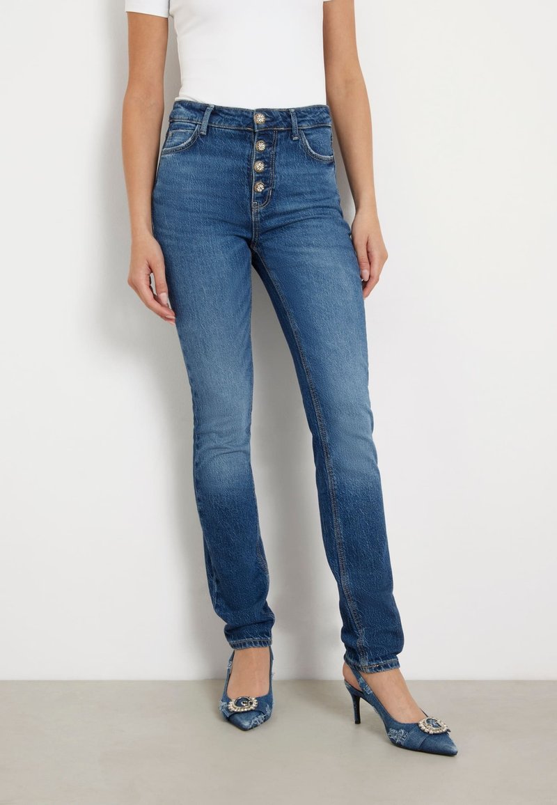 Kõrge vöökohaga sinised denim teksad, millel on kulunud viimistlus, viie esipaknaga ja kitsas sobivus. Kombineeritud terava ninaga kontsadega.