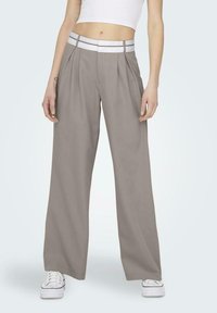 Pantalones de pierna ancha gris claro con una cinturilla blanca y pliegues, hechos de una tela suave. Combinados con zapatillas blancas.