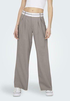 Pantalones de pierna ancha gris claro con una cinturilla blanca y pliegues, hechos de una tela suave. Combinados con zapatillas blancas.
