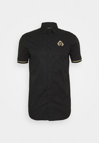 Musta lyhythihainen paita, joka on valmistettu sileästä kankaasta, ja jossa on kultainen symboli vasemmassa rinnassa sekä erottuvat kultaiset raidat hihoissa.