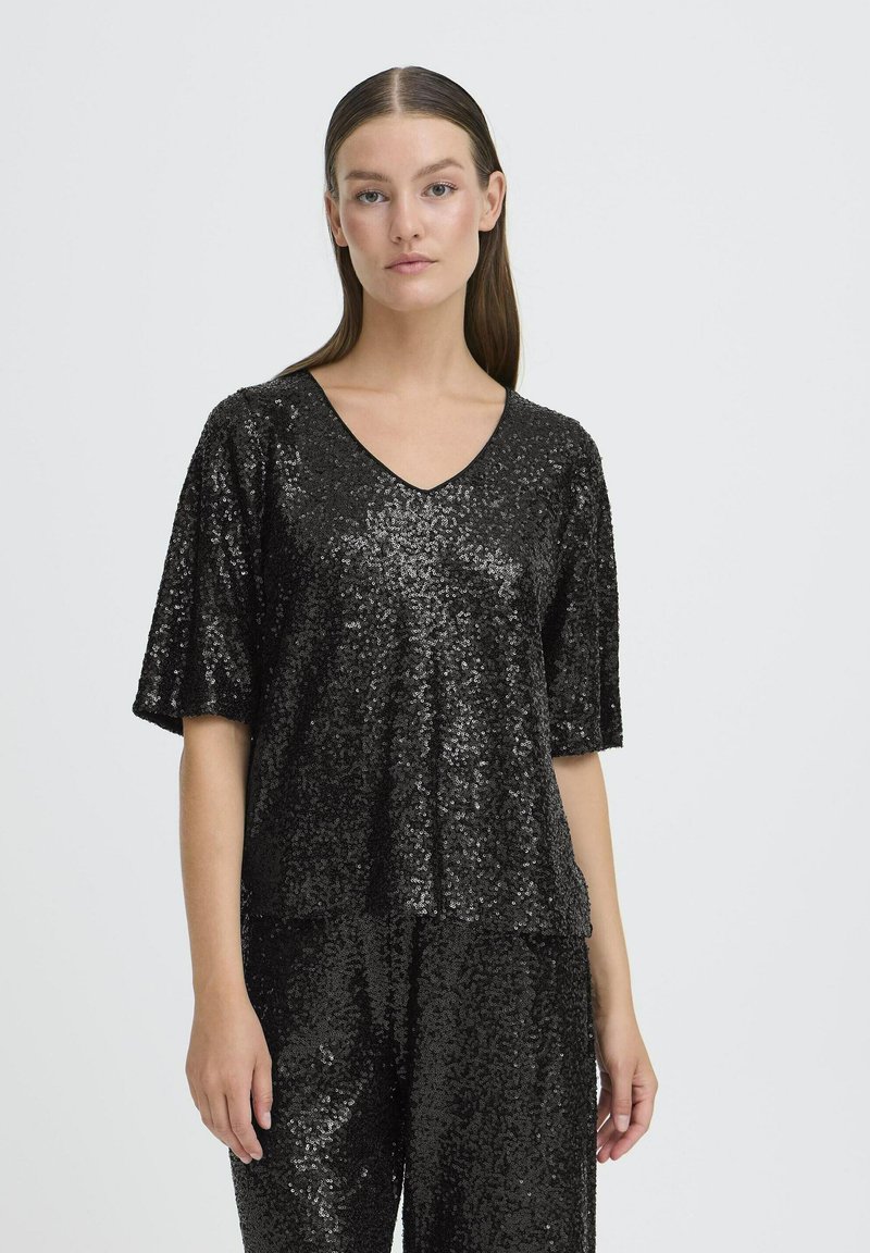 Mustat paljetit-t-paita lyhyillä hihoilla, V-pääntiellä ja väljällä mitoituksella. Ominaisuutena teksturoitu, kiiltävä pinta, joka heijastaa valoa.