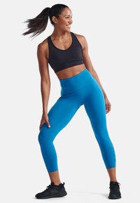 Höga blå leggings och en svart sport-BH gjorda av stretchmaterial, med en slät yta och en figurnära design för träningskläder.