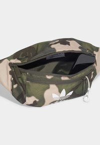 Kamouflage midjeväska i gröna och beige nyanser, tillverkad av ett tyg med en slät yta; har dragkedjestängning och en vit logotyp.