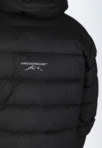 Svart puffjacka med quiltat mönster, med huva och "SWEDEMOUNT"-logotypen i vitt ovanför en bergsgrafik på baksidan.
