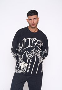 Pulover negru cu modele abstracte albe, guler rotund și mâneci lungi. Fabricat dintr-un material tricotat texturat.