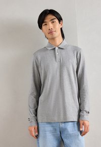 Polo shirt grigio a maniche lunghe con colletto e bottoni, caratterizzato da una texture sottile, abbinato a jeans azzurri chiari.